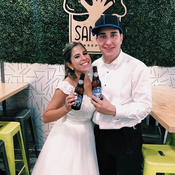 A smiling couple, the woman in a wedding dress, holding Polar beer bottles at Saman.