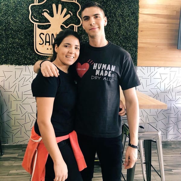 Two smiling Saman employees, a woman and a man, stand arm-in-arm in the restaurant.