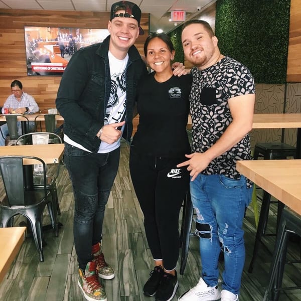 Three smiling people, two men and one woman, pose together inside Saman restaurant.