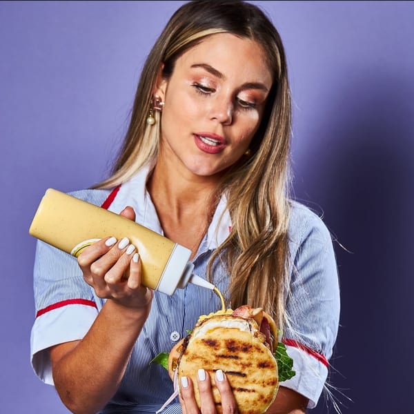 A woman in a striped shirt squeezes sauce onto a Venezuelan arepa filled with egg and bacon.