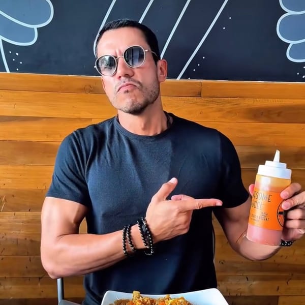 Man in sunglasses pointing at a bottle of "Awesome Sauce" while sitting at a table.